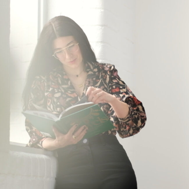 Brand storyteller Siobhan Maher leans against a window, reading a jewellery book.