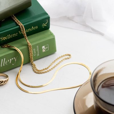 A pile of jewellery books and gold jewellery lies on a window sill.